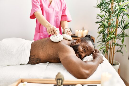 Young african american man smiling confident having back massage with thai bags at beauty center