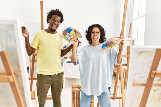 African american artist couple smiling happy holding paintbrush and palette at art studio.