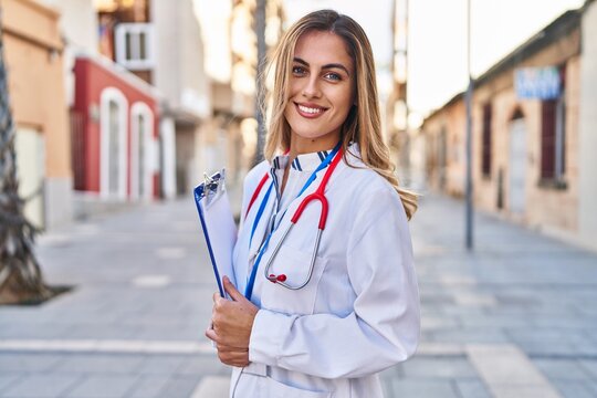 Young blonde woman wearing doctor uniform holding checklist at street
