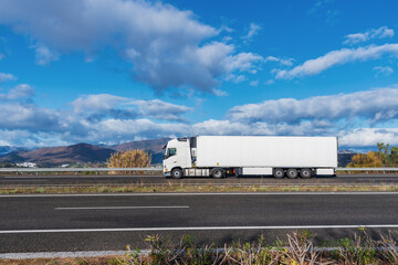 Refrigerated truck driving on the highway seen from the side, with a blue sky with clouds.