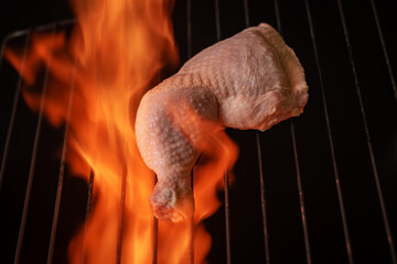 Raw chicken thigh on a grill with fire around it. Foreground.