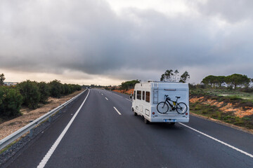 Motorhome with a bicycle hanging at the rear driving on a highway with cloudy skies.