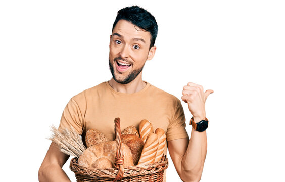Hispanic man with beard holding wicker basket with bread pointing thumb up to the side smiling happy with open mouth