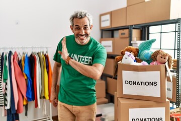 Middle age hispanic man wearing volunteer t shirt at donations stand hand on mouth telling secret...