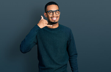 Fototapeta premium Young african american man wearing casual clothes and glasses smiling doing phone gesture with hand and fingers like talking on the telephone. communicating concepts.