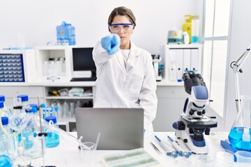 Young hispanic woman wearing scientist uniform working at laboratory pointing with finger to the...