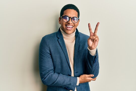 Young handsome hispanic man wearing elegant clothes and glasses smiling with happy face winking at the camera doing victory sign. number two.