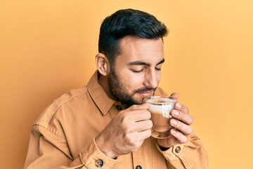 Handsome hispanic man enjoying a cup of coffee over yellow background