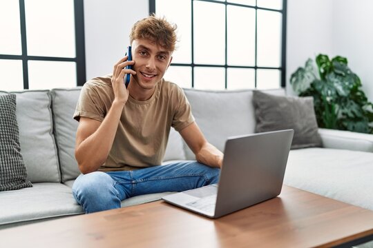 Young caucasian man smiling confident using laptop and talking on the smartphonesmartphone at home