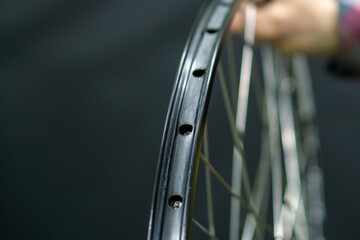 A bicycle mechanic holds a bicycle wheel in his hand on a black background. The rim and the...