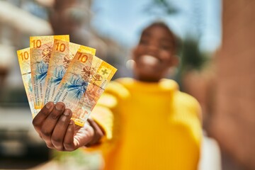 Young african american woman smiling happy holding swiss franc banknotes at the city.
