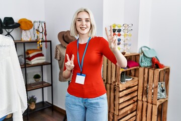 Young caucasian woman working as manager at retail boutique smiling looking to the camera showing fingers doing victory sign. number two.