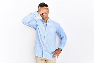 Fototapeta premium Young hispanic man wearing business shirt standing over isolated background smiling and laughing with hand on face covering eyes for surprise. blind concept.