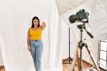 Young beautiful hispanic woman posing as model at photography studio looking unhappy and angry...