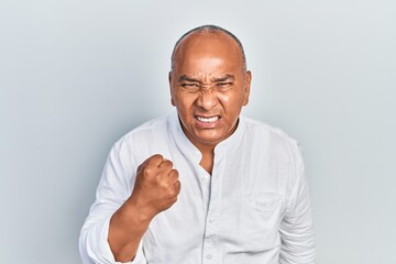 Middle age latin man wearing casual clothes angry and mad raising fist frustrated and furious while shouting with anger. rage and aggressive concept.