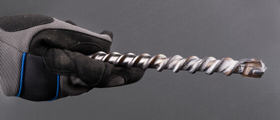Hand with spiral fluted masonry drill bit with carbide tip on a gray background. Closeup of...