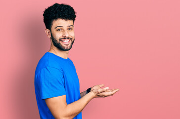 Young arab man with beard wearing casual blue t shirt pointing aside with hands open palms showing...