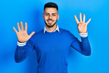 Young hispanic man with beard wearing casual blue sweater showing and pointing up with fingers...