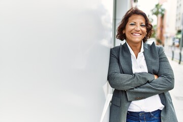Middle age latin businesswoman smiling happy standing with arms crossed gesture at the city.