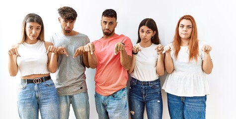 Obraz premium Group of young friends standing together over isolated background pointing down looking sad and upset, indicating direction with fingers, unhappy and depressed.