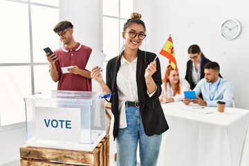Young spanish voter woman smiling happy holding spain flag at vote center.