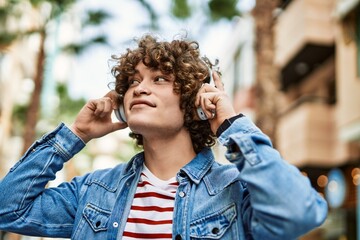 Young hispanic man listening to music wearing headphones at the city