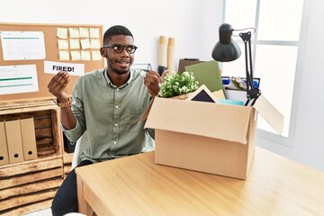 Young african american businessman holding fired banner at the office pointing thumb up to the side smiling happy with open mouth