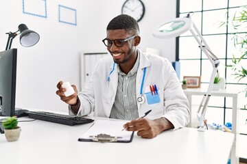 Young african american man wearing doctor uniform holding pills at clinic