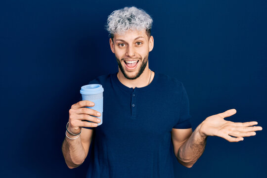 Young hispanic man with modern dyed hair drinking a take away cup of coffee celebrating achievement with happy smile and winner expression with raised hand