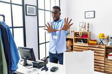 Young african man working as manager at retail boutique afraid and terrified with fear expression stop gesture with hands, shouting in shock. panic concept.