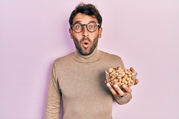 Handsome man with beard holding peanuts scared and amazed with open mouth for surprise, disbelief face