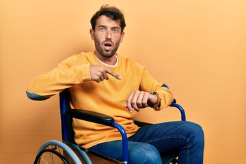 Handsome man with beard sitting on wheelchair in hurry pointing to watch time, impatience, upset...