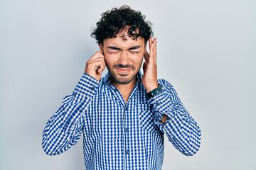 Young hispanic man wearing casual clothes covering ears with fingers with annoyed expression for the noise of loud music. deaf concept.