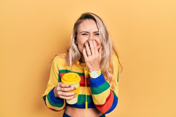 Beautiful young blonde woman drinking cup of coffee wearing headphones laughing and embarrassed...