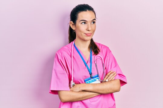 Young brunette woman wearing doctor uniform and stethoscope standing with arms crossed smiling looking to the side and staring away thinking.