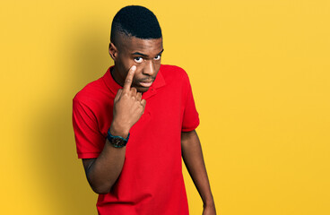 Young african american man wearing casual red t shirt pointing to the eye watching you gesture, suspicious expression - obrazy, fototapety, plakaty
