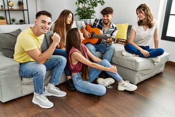 Obraz premium Group of young friends on party playing classical guitar and singing song at home.