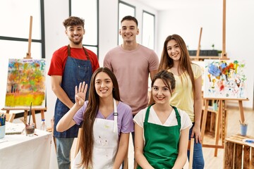 Group of five hispanic artists at art studio showing and pointing up with fingers number four while smiling confident and happy.