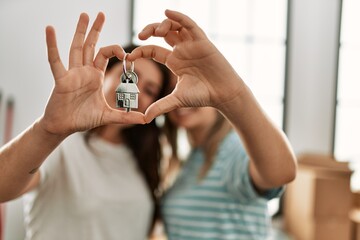 Young couple doing heart symbol with fingers and holding key of new home.