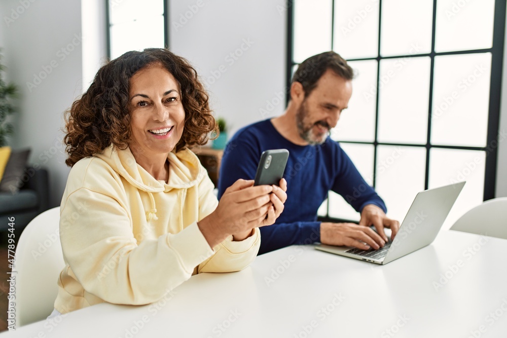 Poster Middle age hispanic couple smiling happy using laptop and smartphone at home.