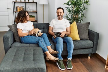 Middle age hispanic couple smiling happy sitting on the sofa with dogs at home.