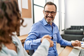 Obraz premium Two middle age business workers smiling happy and shaking hands at the office.