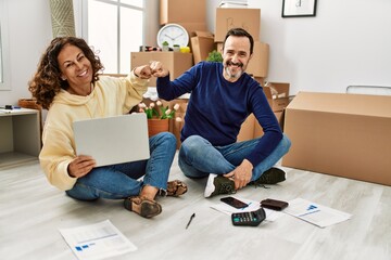 Middle age hispanic couple smiling happy bump fists. Sitting on the floor at new home.