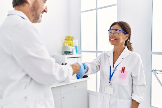 Middle age man and woman partners wearing scientist uniform shake hands at laboratory