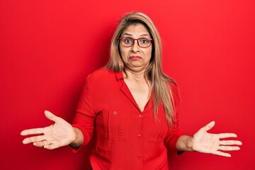 Middle age hispanic woman wearing casual clothes and glasses clueless and confused expression with...