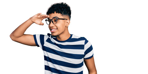 Young african american man wearing casual clothes and glasses very happy and smiling looking far away with hand over head. searching concept.