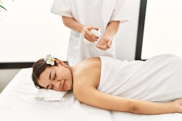 Young latin woman relaxed having back massage with moisturizer at beauty center