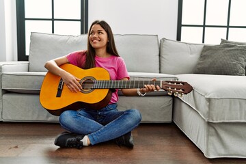 Young latin woman playing classical guitar sitting on floor at home
