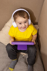 Little caucasian boy with yellow shirt playing game on digital tablet at home. Portrait of a child at home watching cartoon on violet tablet. Modern kid and education technology.