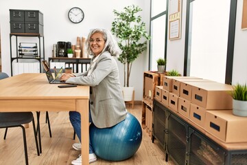 Middle age grey-haired businesswoman sitting on fit ball working at the office.